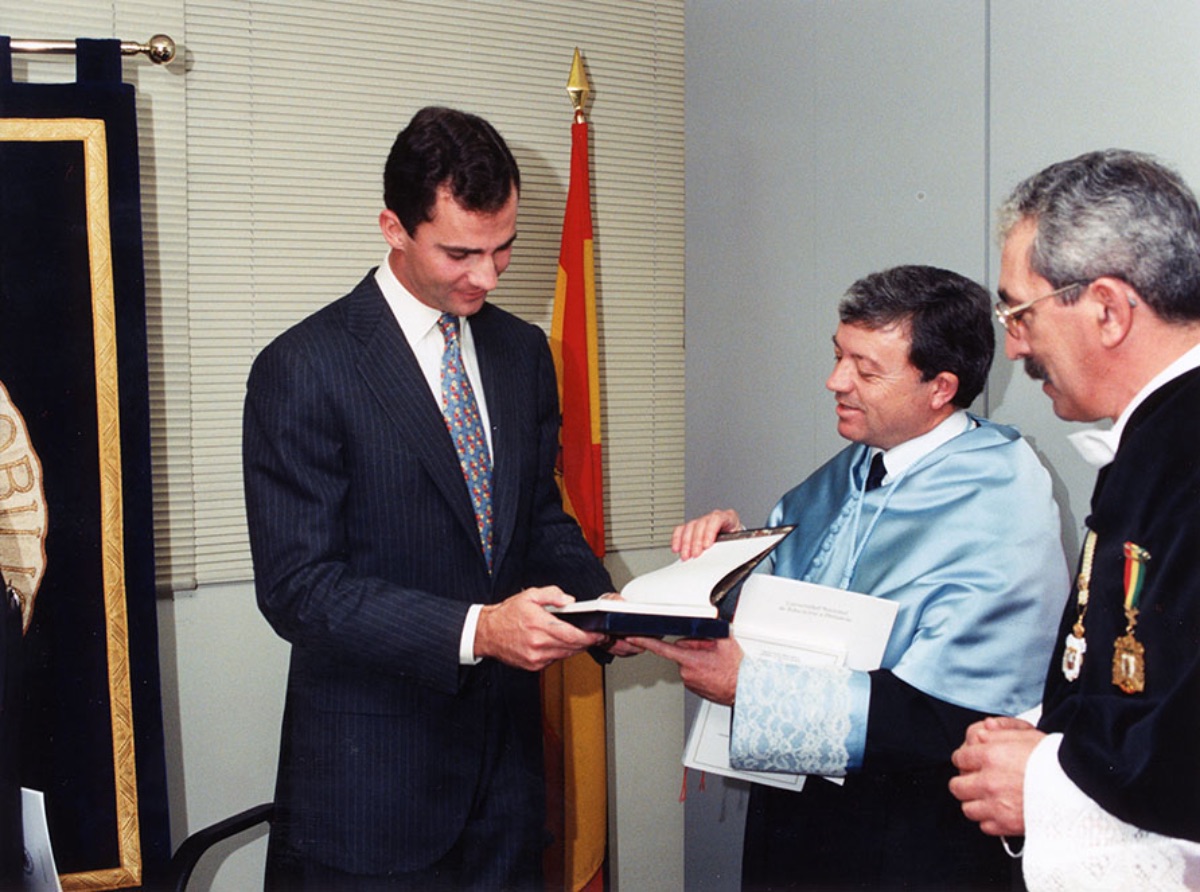 Miguel   Ángel Pérez Priego, Vicerrector de Centros Asociados de la UNED, tiende un   libro al Príncipe Felipe de Borbón. Ante ellos está el Rector Jenaro Costas.