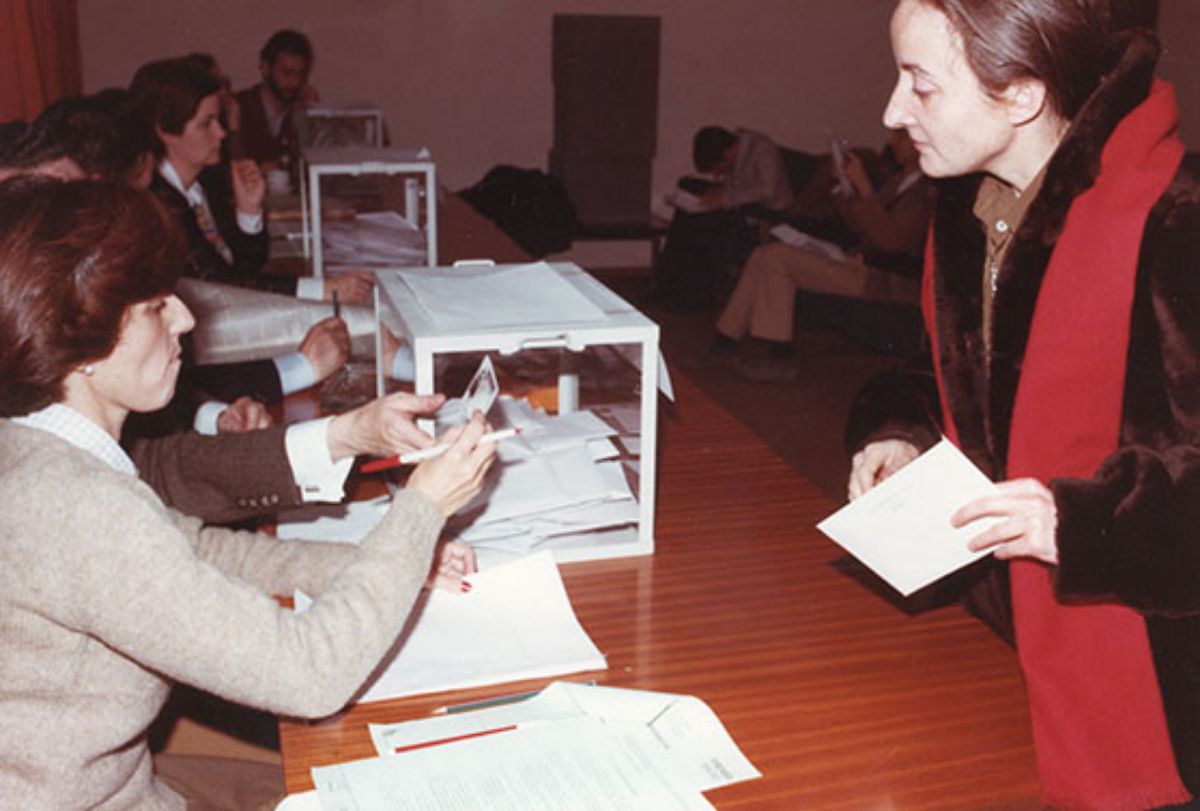 Vista   general de la mesa electoral durante la votación celebrada el 2 de febrero de   1984 para la formación del Claustro Constituyente de la UNED. La imagen   recoge el momento en que una mujer se dispone a votar (1984)
